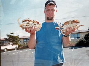 Man in blue shirt and cap holding two large Dungeness crabs in parking lot