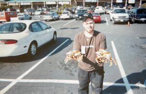 Man holding two large Dungeness crabs in shopping center parking lot with cars in background