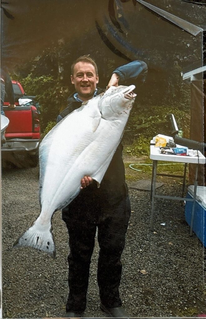 Angler holding large halibut at dock with boat hull and cleaning table visible in background