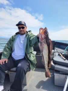 Angler on boat holding large lingcod by the mouth with ocean and clouds in background