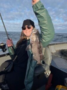 Angler holding lingcod on fishing boat with ocean and cloudy sky in background