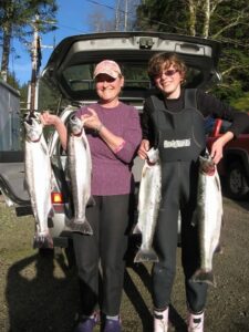 Two anglers in wetsuits display six coho salmon at vehicle tailgate after fishing trip