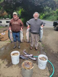 Two anglers display four chinook salmon and several Dungeness crabs at riverside campground with RV