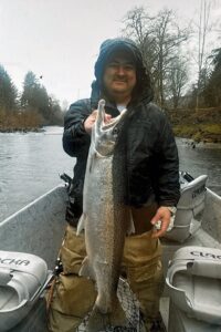 Angler in dark jacket holding large chinook salmon on aluminum fishing boat in rainy winter conditions
