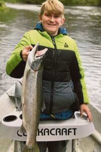 Young angler holding large chinook salmon while sitting in white kayak on river water.