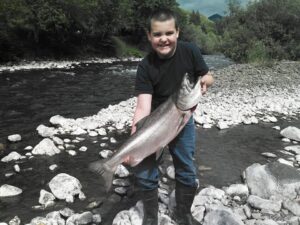 Young angler holding large chinook salmon while standing in rocky river shallows in Oregon