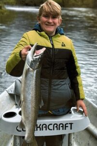 Young angler in yellow jacket holding large chinook salmon while kneeling in white kayak on river