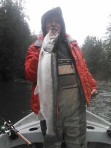 Angler in red rain jacket holding fresh coho salmon on boat in misty river conditions