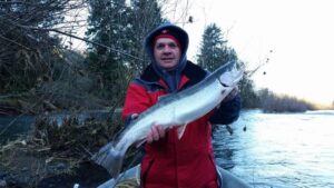 Angler in red jacket holding silver coho salmon while standing in boat on winter river.