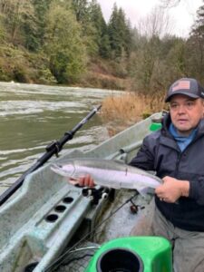 Angler in drift boat holding silver coho salmon on forested river in winter conditions