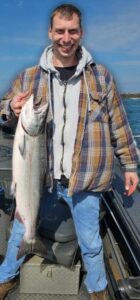 Angler on boat holding large steelhead trout with gray hooded sweatshirt and plaid shirt