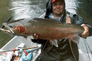 Angler in boat holding large steelhead with bright pink stripe along lateral line in river setting