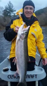 Angler in yellow jacket holding large steelhead from boat on overcast river day