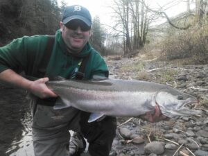 Angler in green hoodie and Detroit cap holding large steelhead on rocky riverbank
