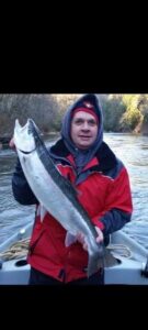 Angler in red jacket holding large silver salmon while standing in boat on river