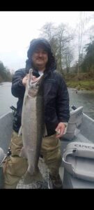 Angler in hooded jacket holding large salmon while standing in drift boat on misty river