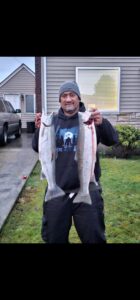 Angler holding large salmon in residential driveway on overcast day with house and vehicle in background