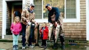 Two adults and two children displaying four salmon in front of a house entrance
