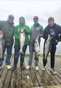 Four anglers on wooden dock displaying multiple large chinook salmon on overcast day