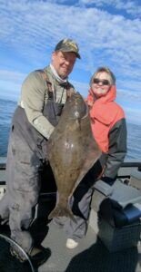 Two anglers on boat holding large halibut on calm ocean day with blue sky and clouds