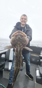 Angler on boat holding large lingcod by mouth in foggy ocean conditions